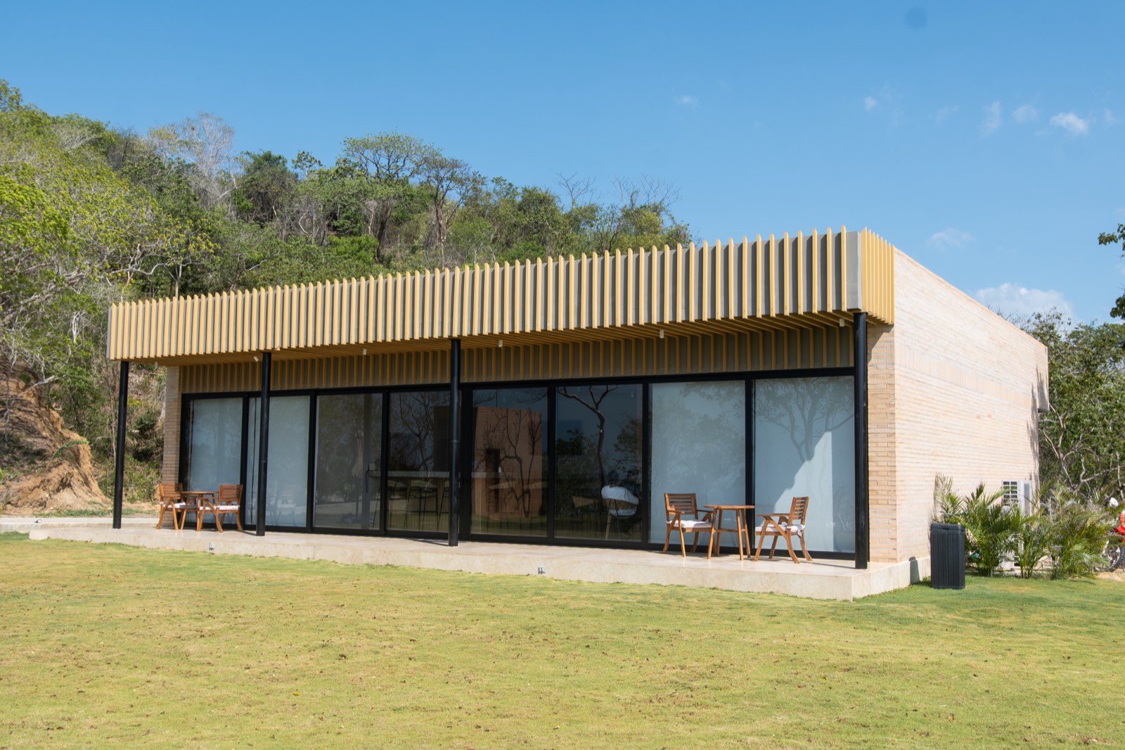 La casa club del proyecto, con ventanales y alero de listones de madera sobre el prado